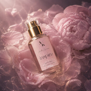 Pink perfume bottle labeled 'inspire' nestled among pink peony petals on a soft, dreamy background.
